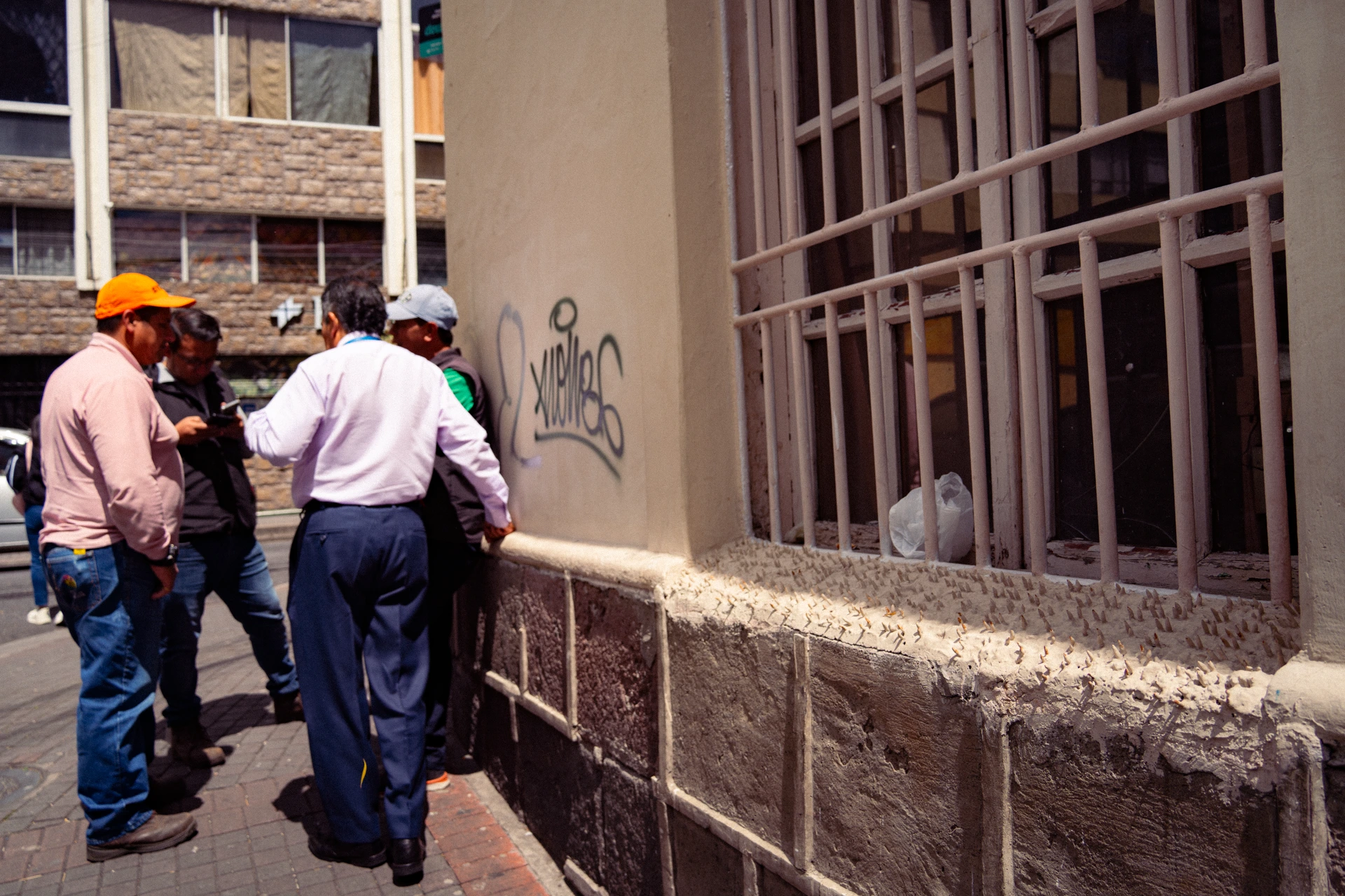 Un grupo de hombres conversa arrimados a la parte de la pared que no tiene pinchos