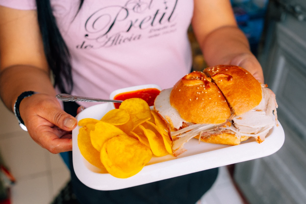 El sánduche viene en un plato blanco con ají y papas fritas de funda.
